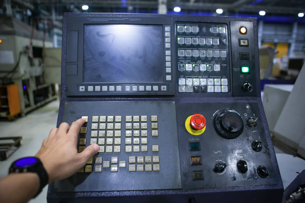 Operator interacting with an industrial CNC machine control panel, featuring a keypad, function buttons, display screen, and emergency stop button.